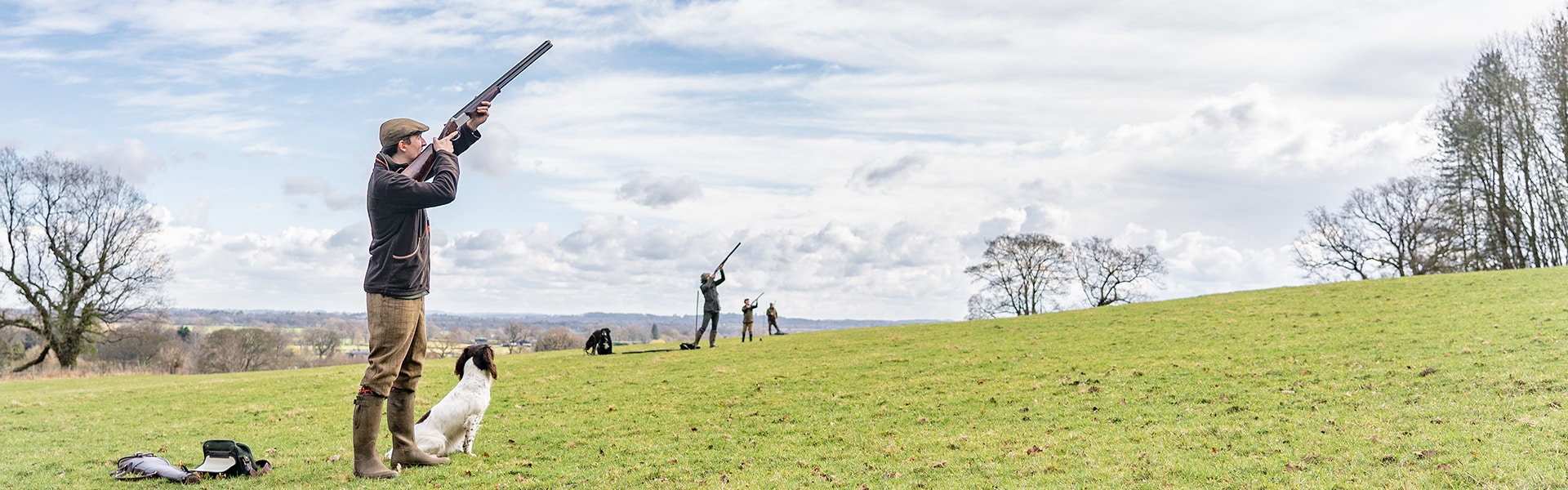 A shooter in a field with their gundog taking aim