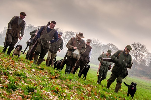 A group of shooters walking with their dogs through a field