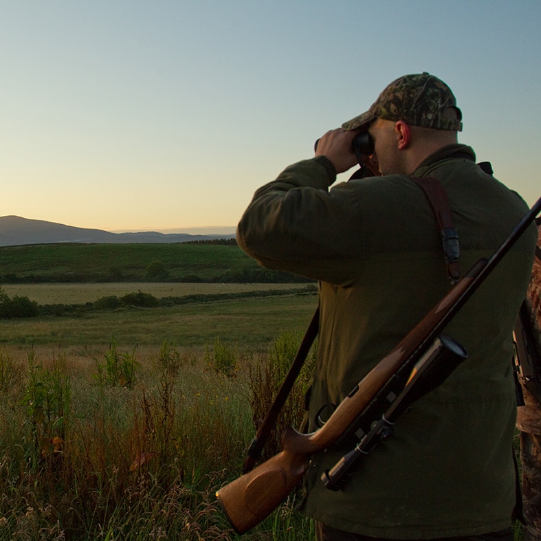 A deer stalker looking through their binoculars