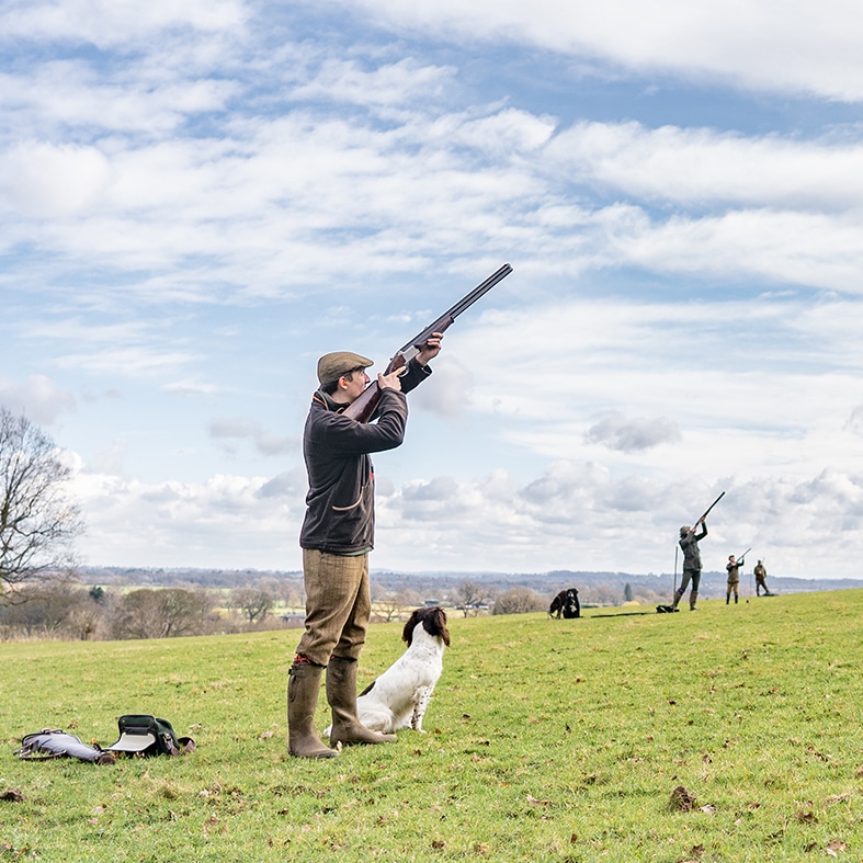 A shooter in a field with their gundog taking aim