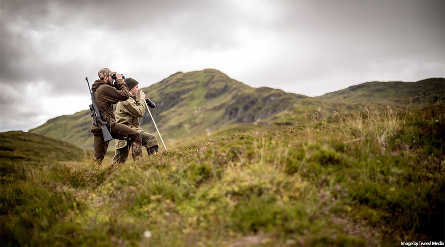 Two deer stalkers looking through binoculars on a hill side