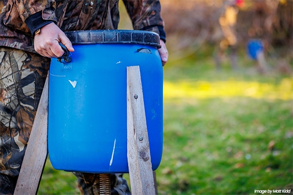 A gamekeeper placing a plastic barrel on the floor