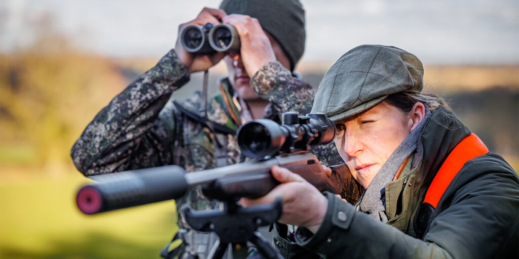 Shooter aiming down a scope of a sound moderated rifle